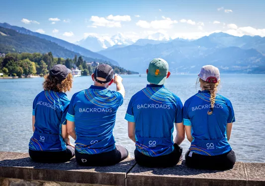 Four guests looking out towards lake, pointing to mountains.