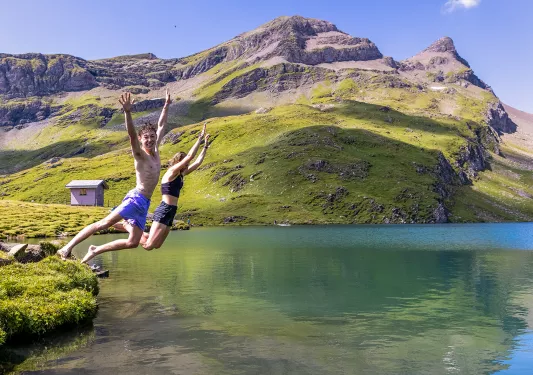 Two guests jumping into small lake, sharp cliffs and small shack in background.