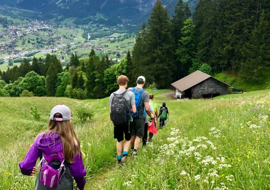 Group of guests hiking towards small rocky shack, large valley town and mountain range in distance.