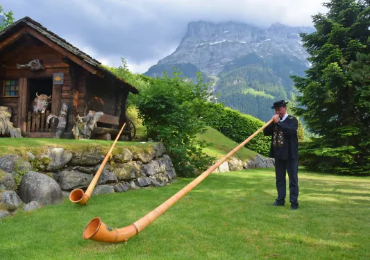 Local man playing a Swiss Horn, wooden shack in background.