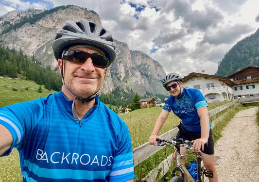 Guests taking selfie, hotel and mountain range in background.