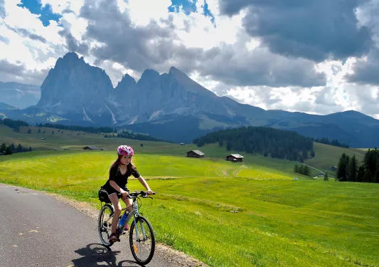 Young guest cycling down mountain road, large range and meadow in background.