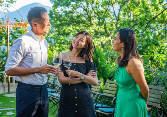 Three guests on grassy terrace. Two have wine glasses.