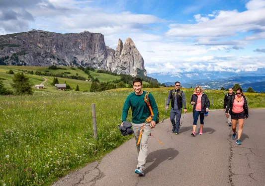 Five guests walking up hillside road, large cliffs, small houses in distance.