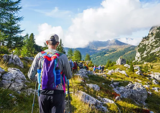 Group of guests hiking down mountain trail, cloudy mountainous vista in distance.