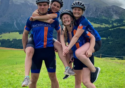Four young guests posing for camera, two on the other two's backs, mountains in background.