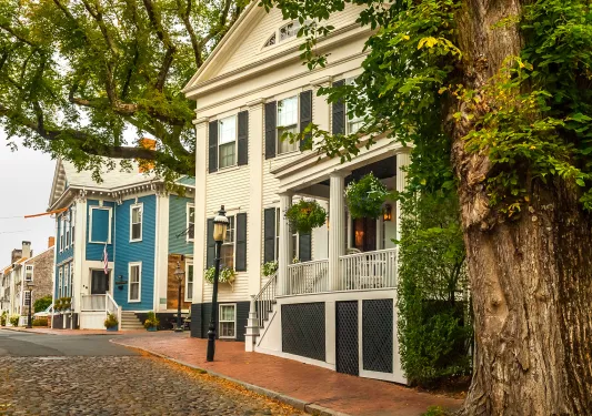 Shot of a residential street, two large, multi-room houses visible.
