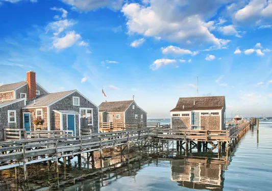 Shot of three small houses on the water, pier and small boat in background.