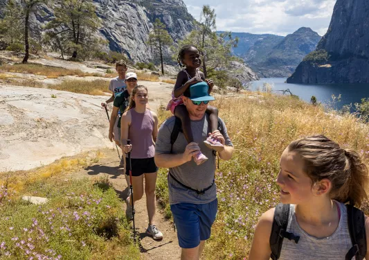 Hiking family, stream to their left, mountains in background.