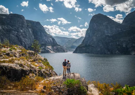 Two guests embracing in front of a large lake, blue sky and mountain in background.