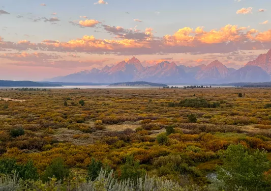Purple and orange sunset with scenic green field and rocky mountains