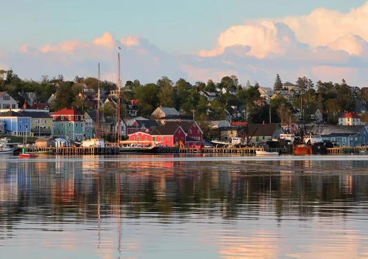 Wide shot of seaside town at sunset, vibrant red houses scattered throughout.