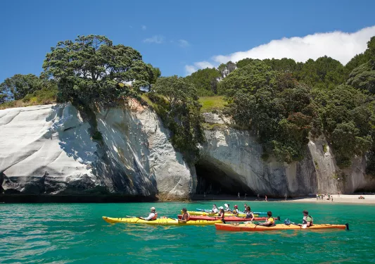 Guests kayaking away from beach, white stone cliff behind them. 