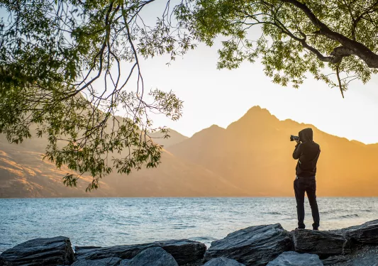 Single hiker taking a photo at the edge of a lake in New Zealand