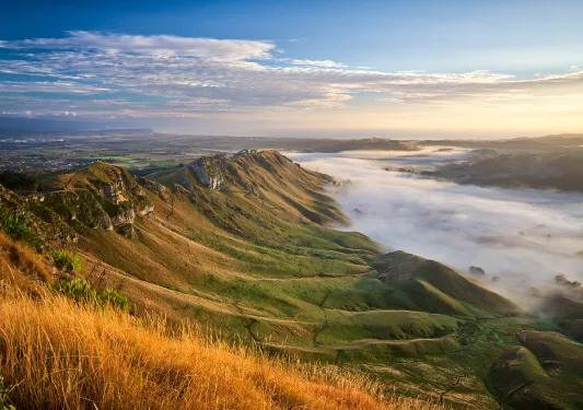 Wide shot of cloud covered valley during sunset, sloping cliffs rising from it.