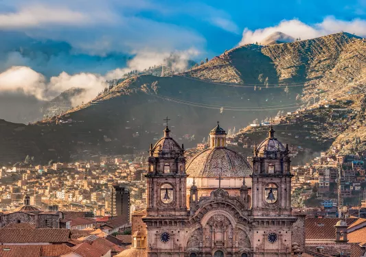 Wide shot of South American city, mountain range in distance, large cathedral in foreground. 
