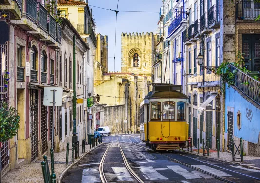 Street shot of Lisbon, Portugal. Tram, colorful buildings, stone tower in distance. 