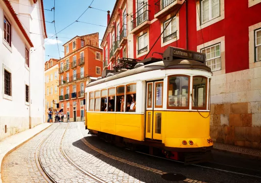 Shot of yellow trolley car on street, red houses around.