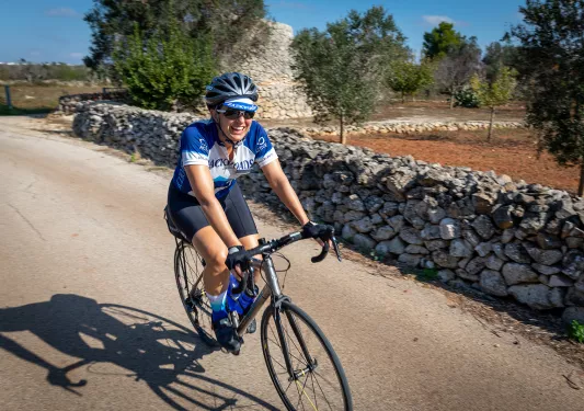 Guest cycling down road, rocky wall and tree farm on left.