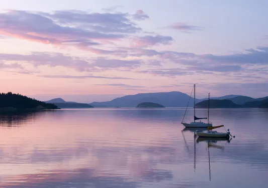 Two sailboats on a still lake during purple sunset.