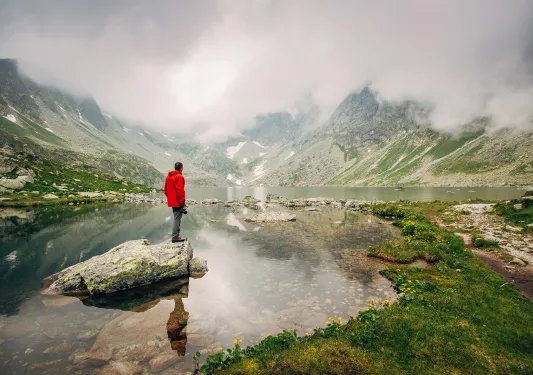 Man in red coat standing in middle of misty lake.