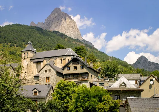 Shot of mountainside town, large stone buildings in treeline, mountain above.