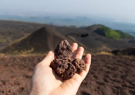 Point of view shot of volcanic rock landscape, hand holding volcanic rocks.