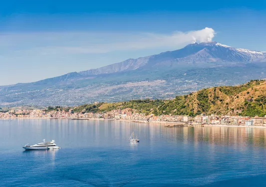 Wide shot of Mount Etna, small boats in water in foreground.