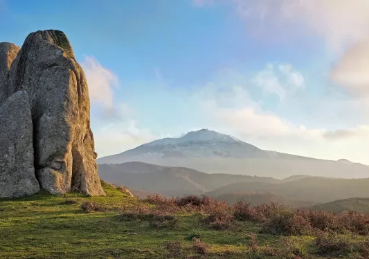 Shot of large rock face, mountains, sunset in distance.