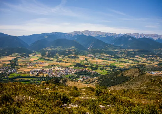 Bird's eye shot of mountainous valley, town, golden fields below.