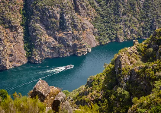 Hillside shot of craggy river valley, passenger boat in water below.
