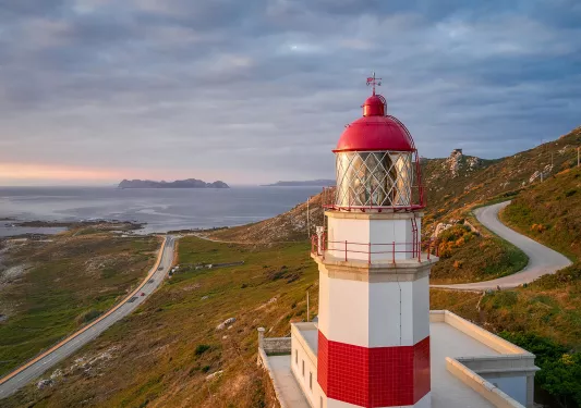 Wide shot of Spanish coastline during sunset, red and white lighthouse in foreground.