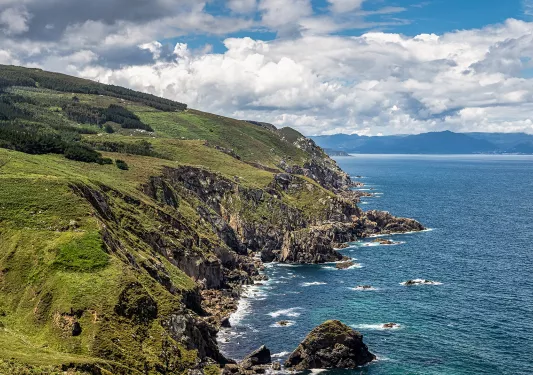 Shot of green, craggy coastline, ocean to right.
