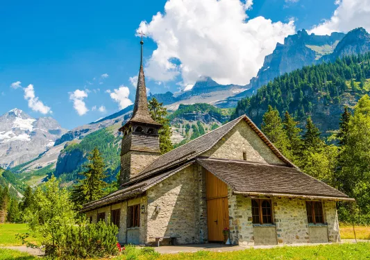Wide shot of stone cathedral, mountains, clouds in distance.