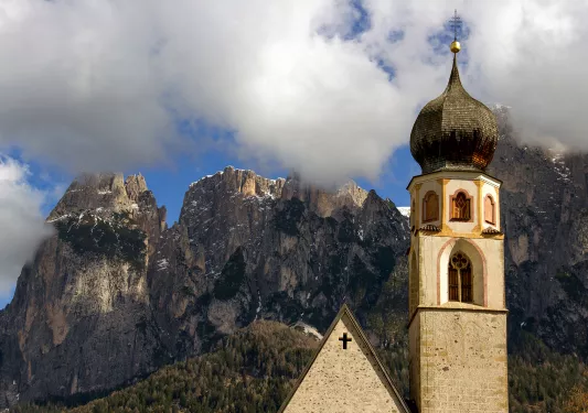 Close-up of church, cloudy mountain tops in background.