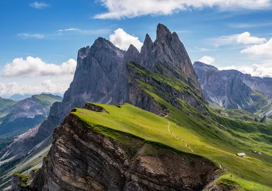 Wide shot of craggy, sharp mountain peaks, small house barely visible.