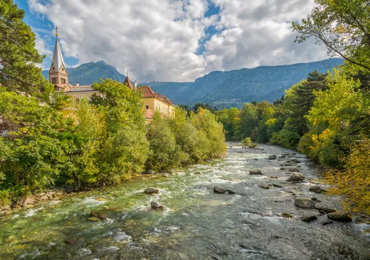 River flowing through forest, stone building on it's left.