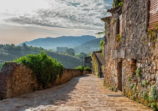 Shot of rocky mountain buildings, verdant hillside in distance. 