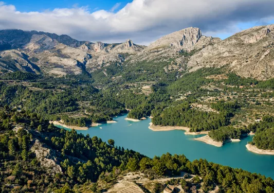Wide shot of mountain valley, blue river running through, trees below.