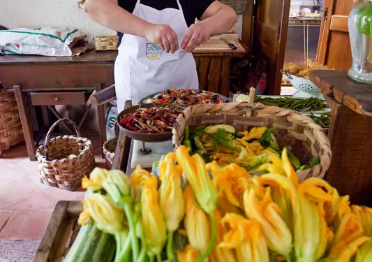 Local chef preparing food, zucchini + blossoms in foreground. 