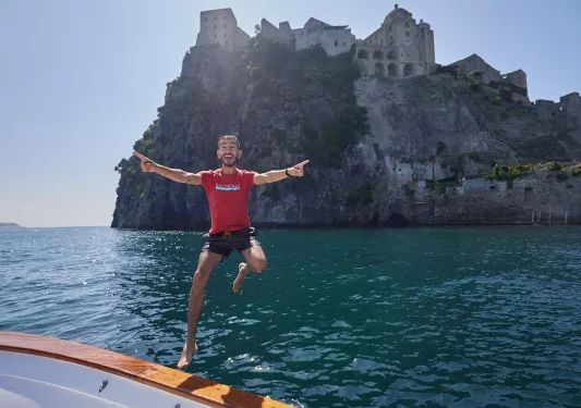 Guest jumping off boat, hilltop house in background.
