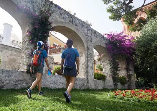 Two guests walking through arched garden. Red and purple flowers.