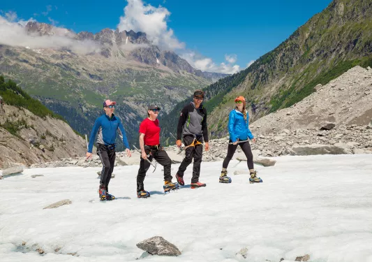 Four guests walking in snow, sweeping mountain range in background.