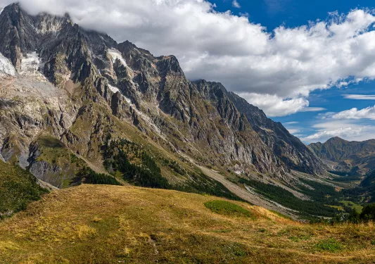 Wide shot of craggy mountains, golden hills in foreground. 