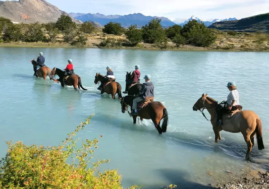 Group of guests on horseback, trekking through cloudy lake.