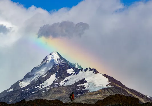 Shot of guest looking towards snowy mountain, rainbow behind it.
