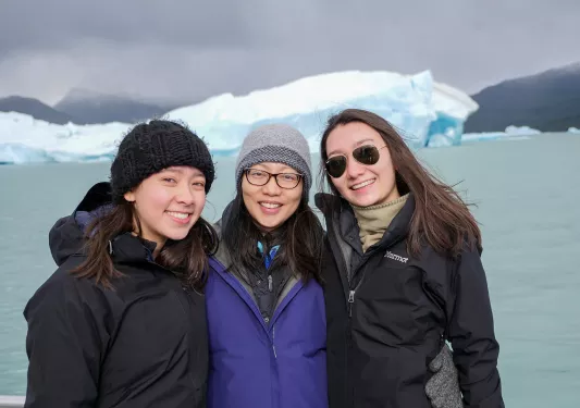 Three young guests smiling, large lake and glacier behind them.