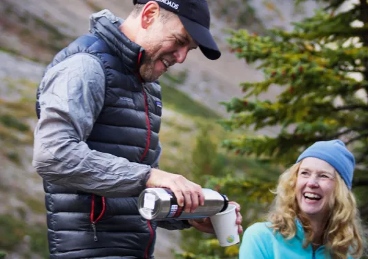 Two guests resting, one pouring beverage, both laughing.