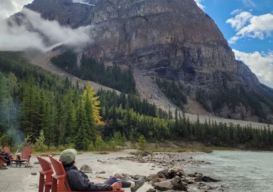 Guest sitting on sandy lakeshore, large mountain in distance.