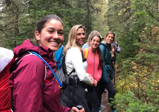Four guests walking forest trail, all smiling at camera.